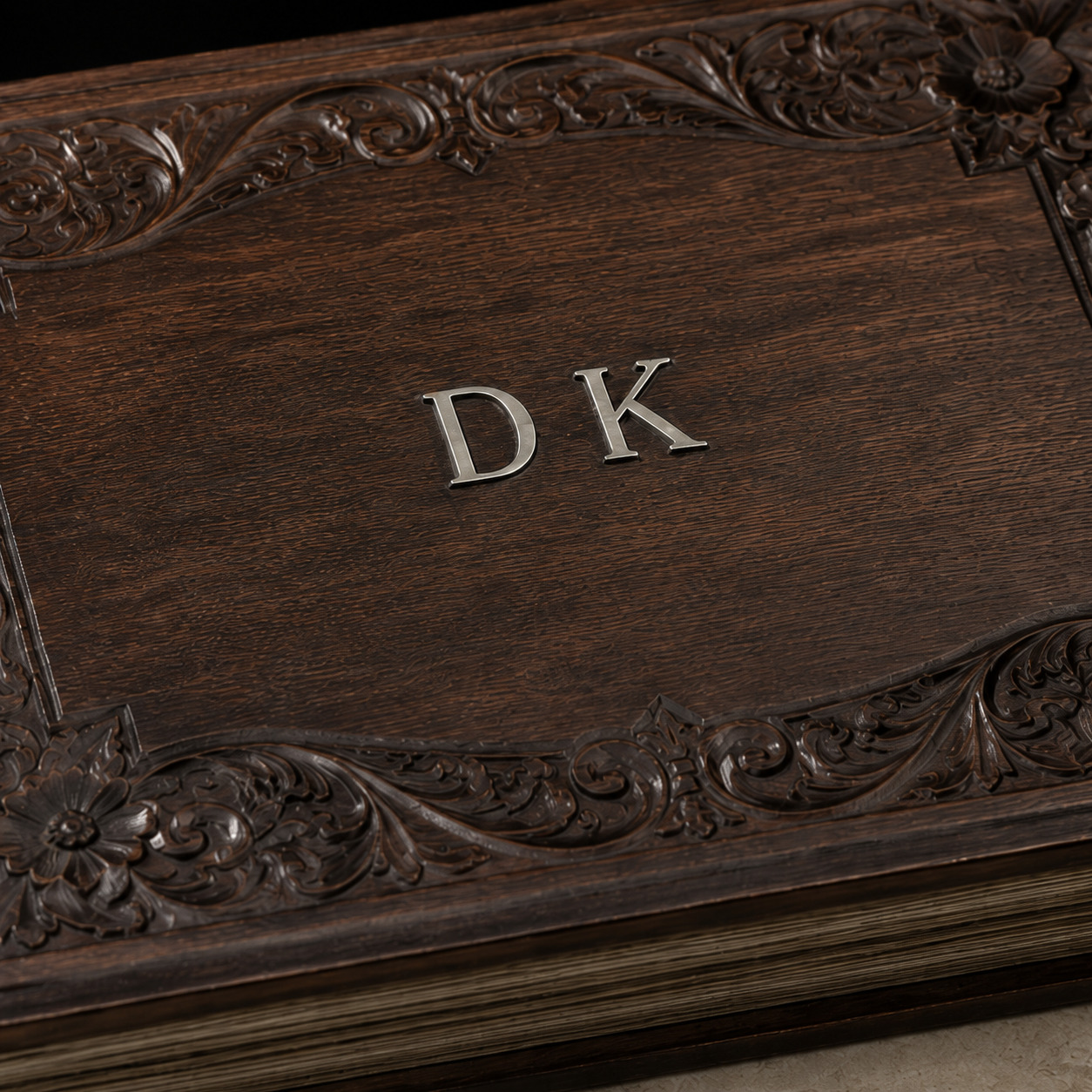 Editorial detail of silvered D K initials mounted on a dark carved wooden album cover.